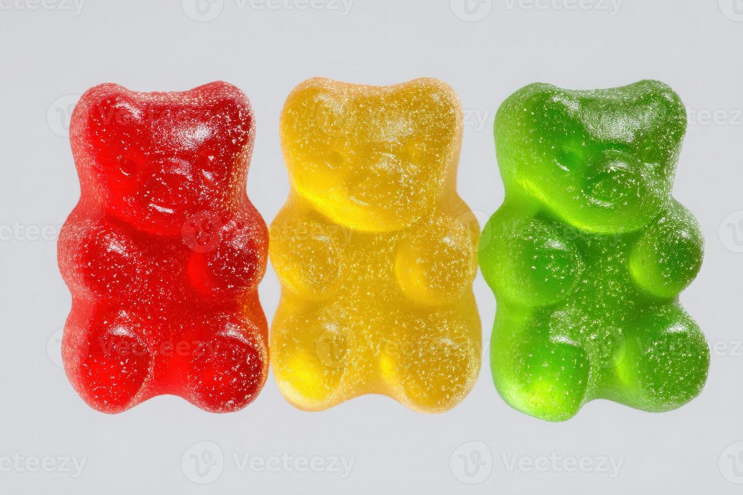 Bright gummy bears in red, yellow, and green sit side by side against a plain backdrop. Their glossy texture and cheerful colors create an inviting and playful visual appeal. photo