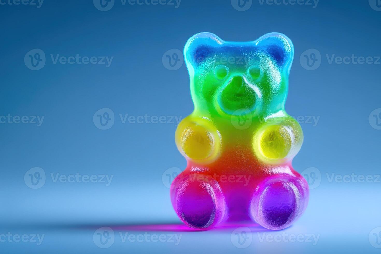 A vibrant gummy bear, featuring a rainbow of colors, sits on a smooth surface with a blue backdrop. The candys playful shape and glossy texture create an eye-catching visual delight. photo