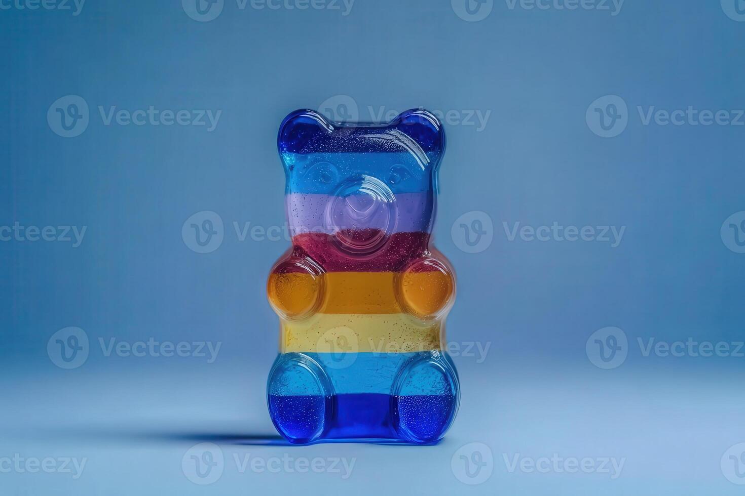 A vibrant gummy bear is displayed prominently, showcasing a mix of colors including red, orange, yellow, and blue against a soft blue background. The bear appears glossy and inviting. photo