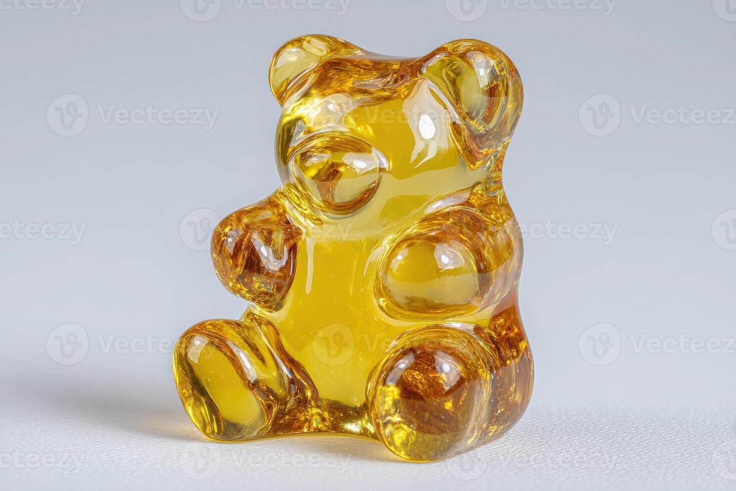 A shiny gummy bear, made of a vibrant yellow substance, sits upright and looks playful. Its rounded features and smooth surface reflect light, creating a cheerful appearance. photo