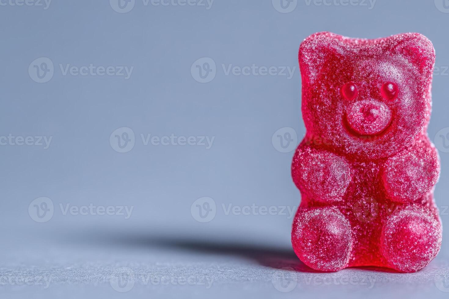 A vibrant red gummy bear candy rests on a sleek surface, illuminated by gentle lighting that enhances its sugary texture. The cheerful figure radiates a playful and inviting charm. photo
