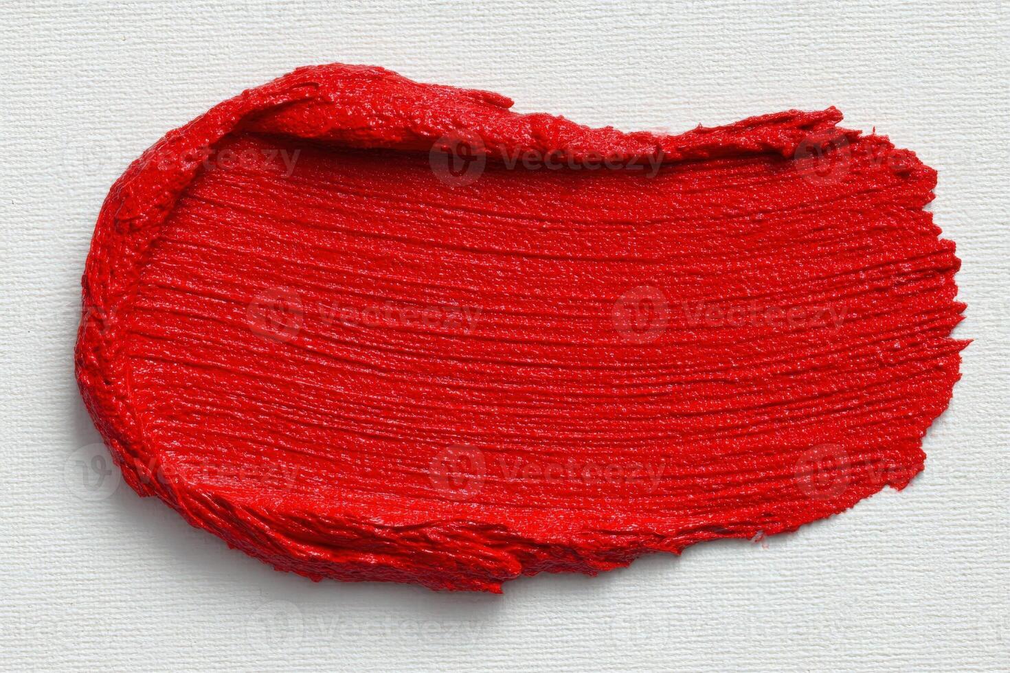 A bold red paint stroke is spread smoothly across a textured canvas background, showcasing a rich and glossy finish. The vivid color highlights the dynamic potential for artistic creation. photo