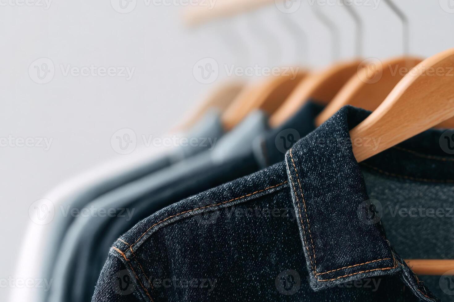 A selection of denim shirts, varying in shades from dark to light, is neatly displayed on wooden hangers. The hangers are arranged in a row against a neutral backdrop, emphasizing the textile details. photo