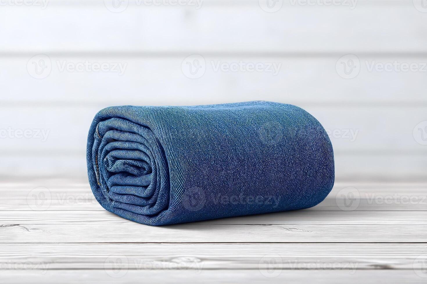 A soft, blue blanket is rolled neatly on a light wooden surface. The texture appears inviting, suggesting warmth and comfort, ideal for a cozy atmosphere. photo