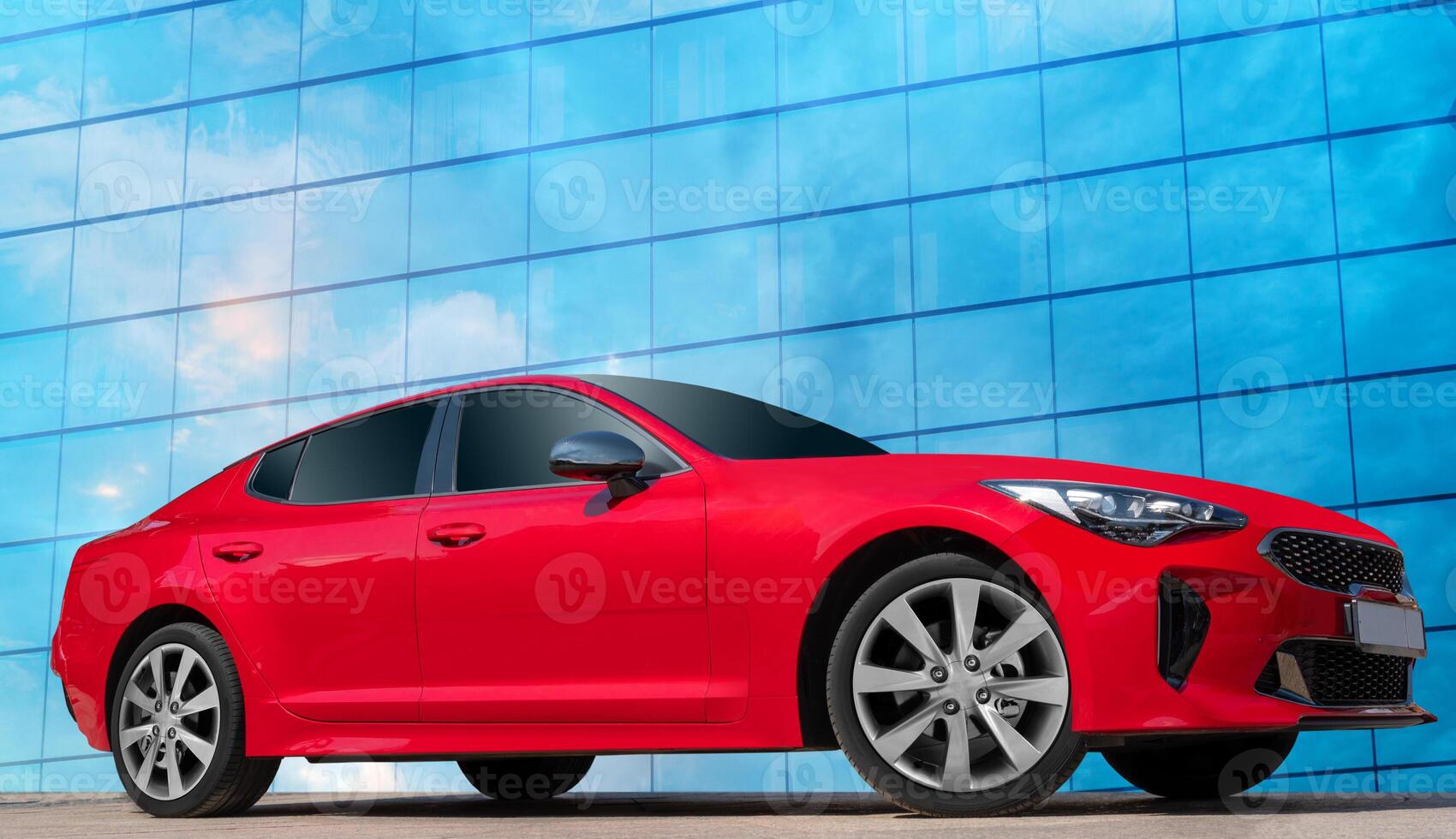 Red car against the blue sky with white clouds reflected in a glass building. Stylish, modern, bright image of a car for design solutions. photo