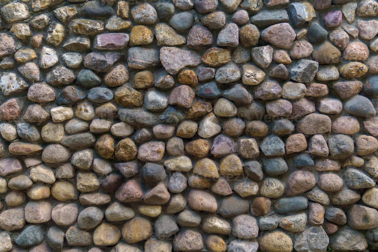 Wall fence of stones of different sizes roughly stacked on top of each other and fastened with cement. Construction industrial background. photo