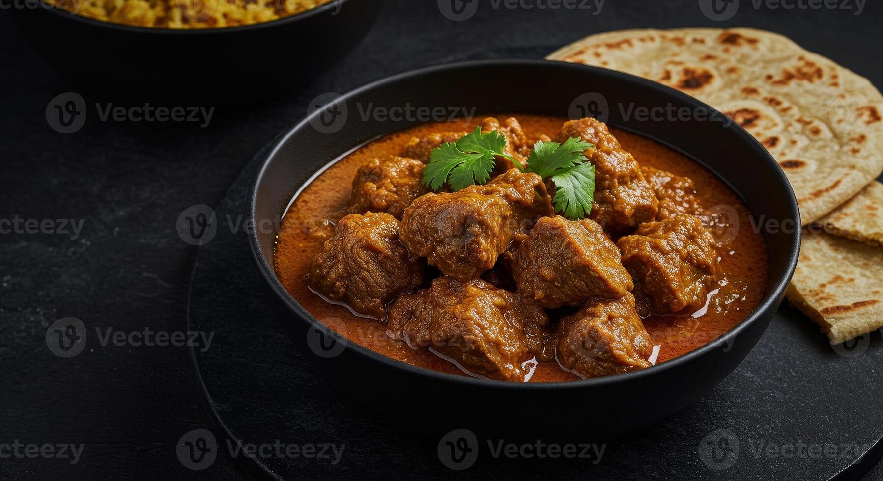 Spicy Caribbean goat curry served in a black bowl with cilantro garnish and roti bread on side photo