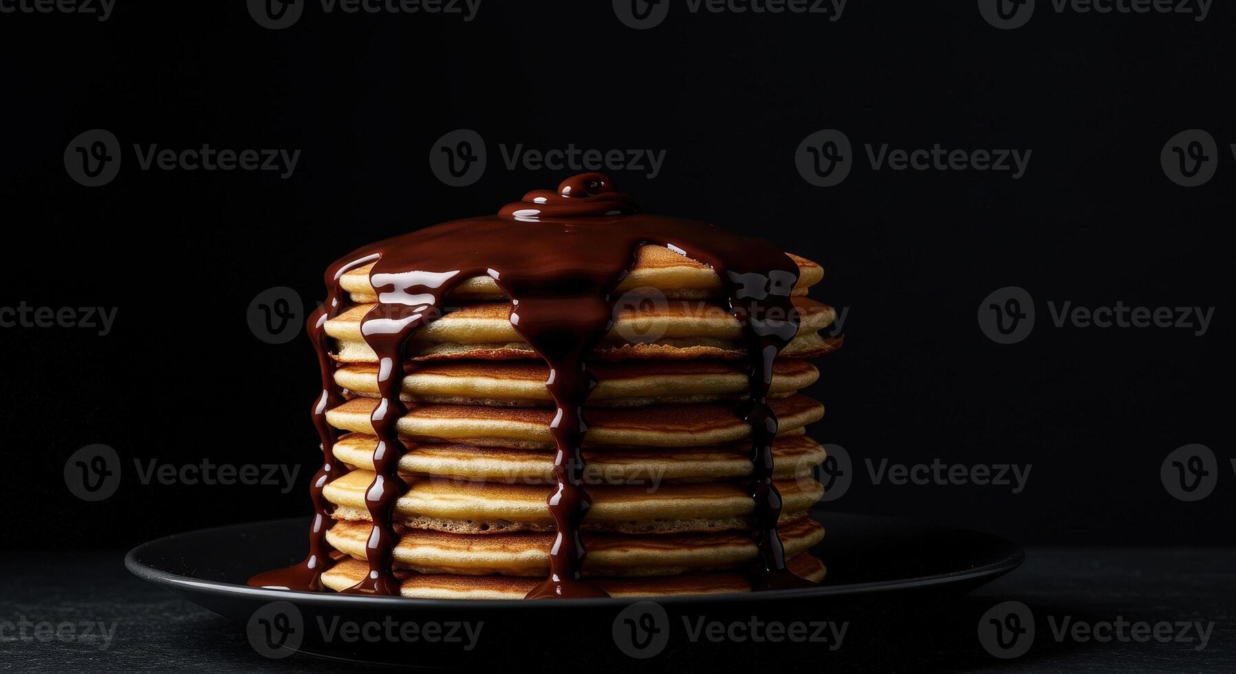Tall stack of fluffy pancakes generously drizzled with rich dark chocolate syrup on black plate photo