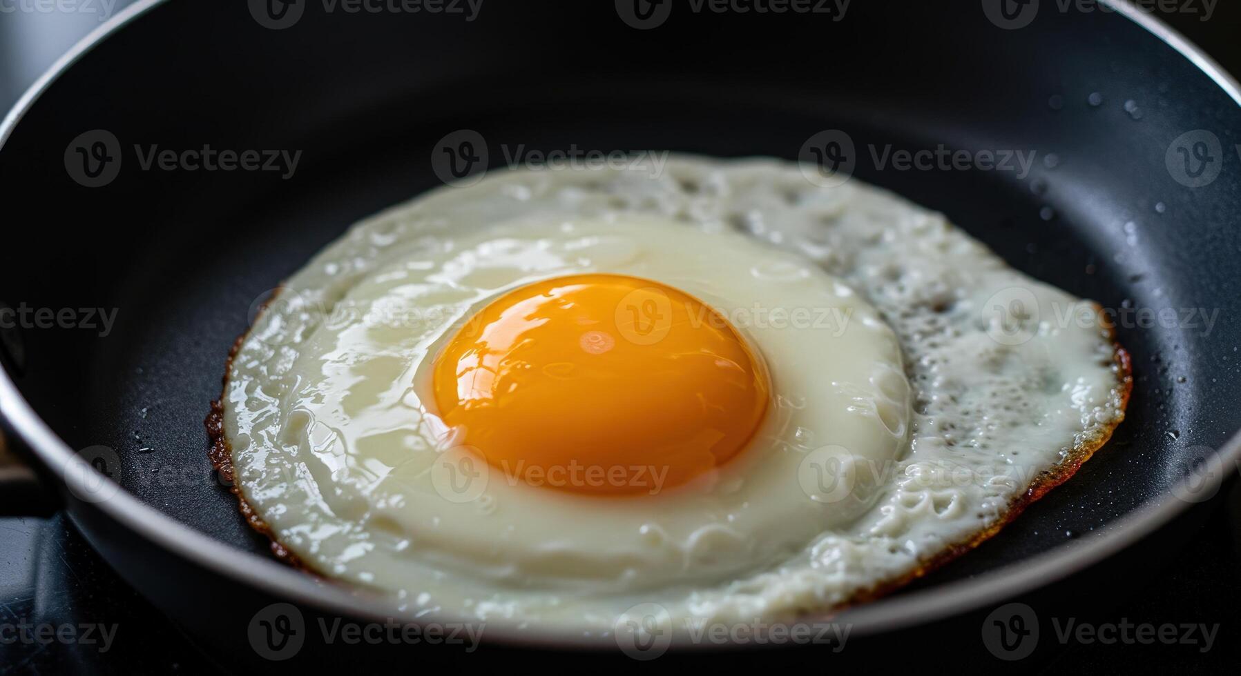 Single fried egg sunny side up with bright orange yolk cooking in dark nonstick pan close up photo