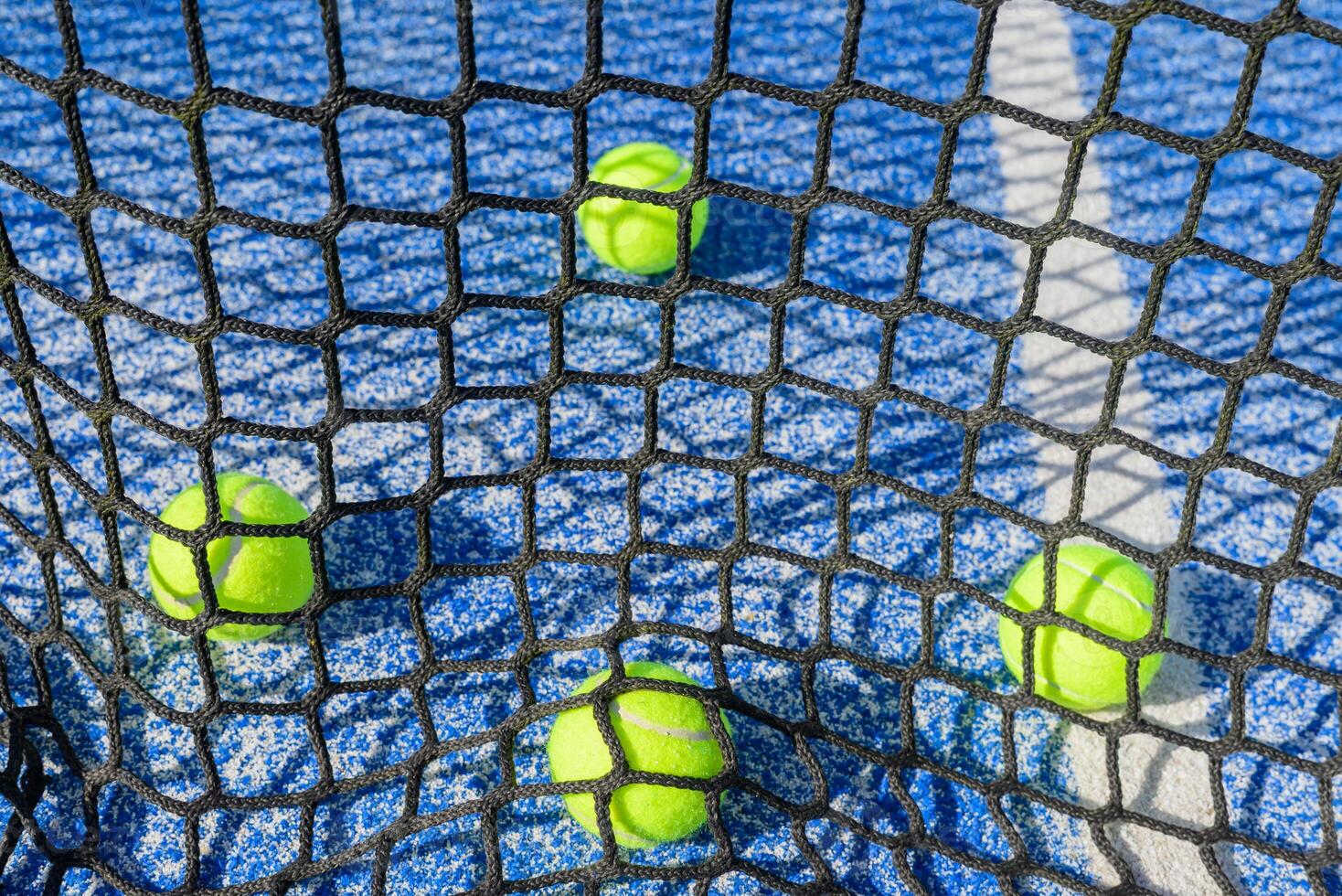 close up of padel court net and scattered balls vibrant colors of a padel tennis court outdoor shadows from padel net on blue court photo