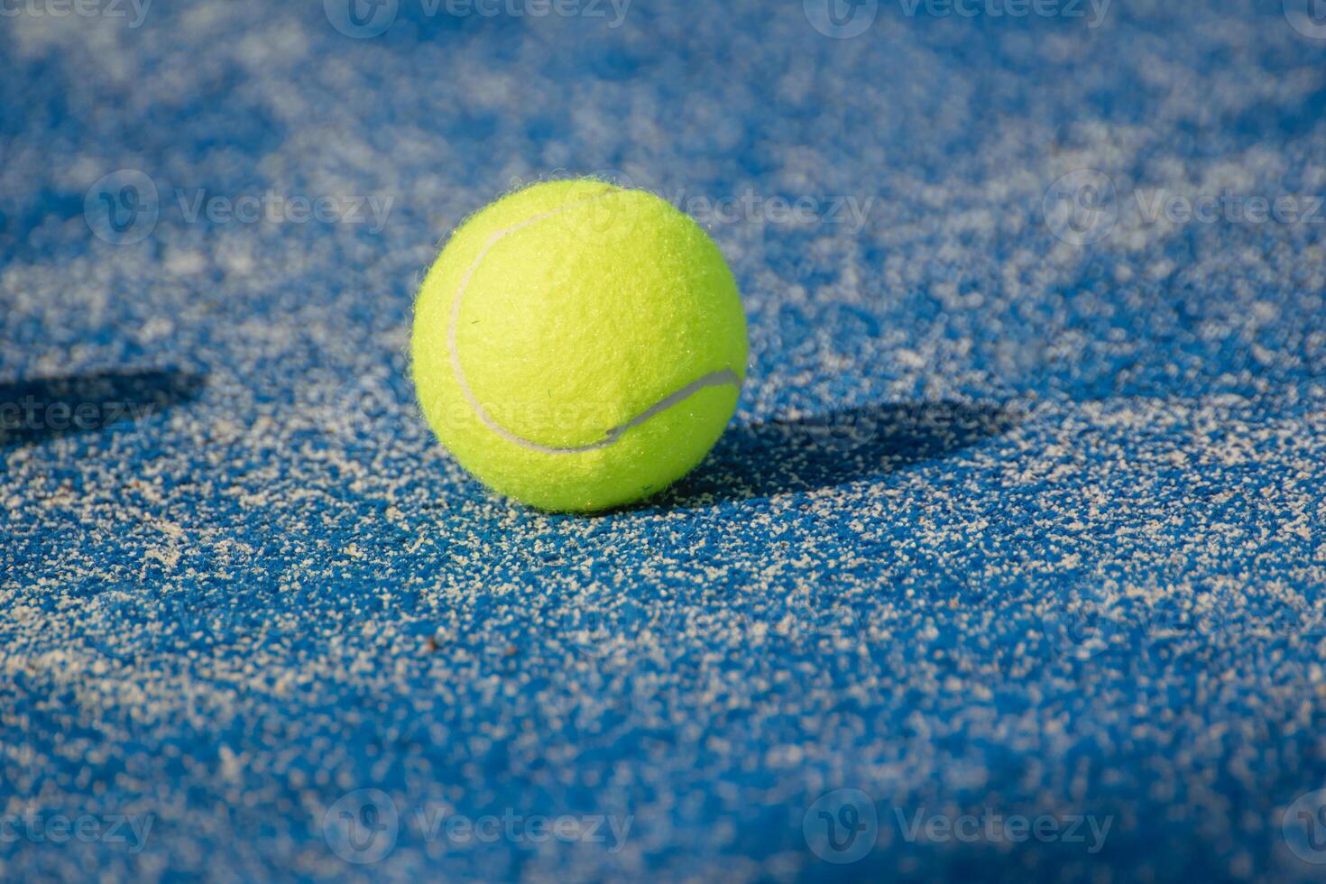 a bright yellow isolated tennis ball on a blue sports ground under net shadow photo