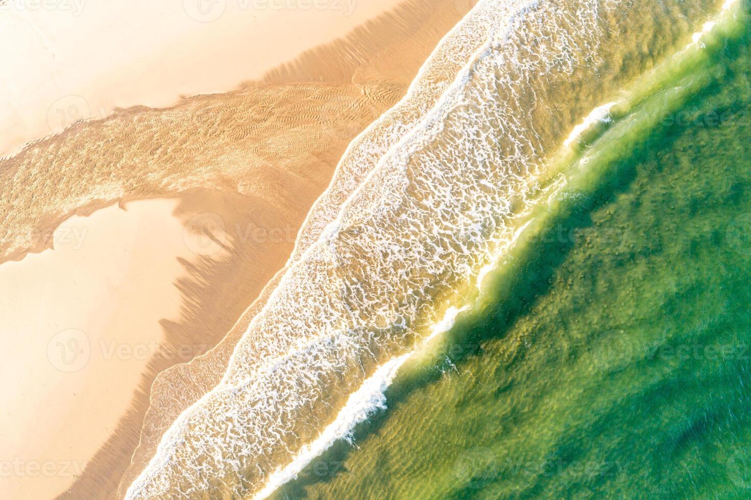 aerial top down drone view over a tropical beach with turquoise water, golden sand, foamy waves at sundown photo