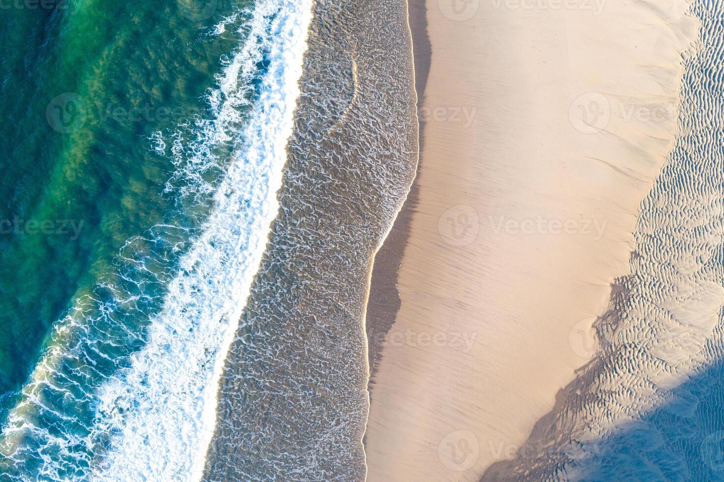 abstract pattern of white breaking waves on a golden sand beach from above aerial drone view photo