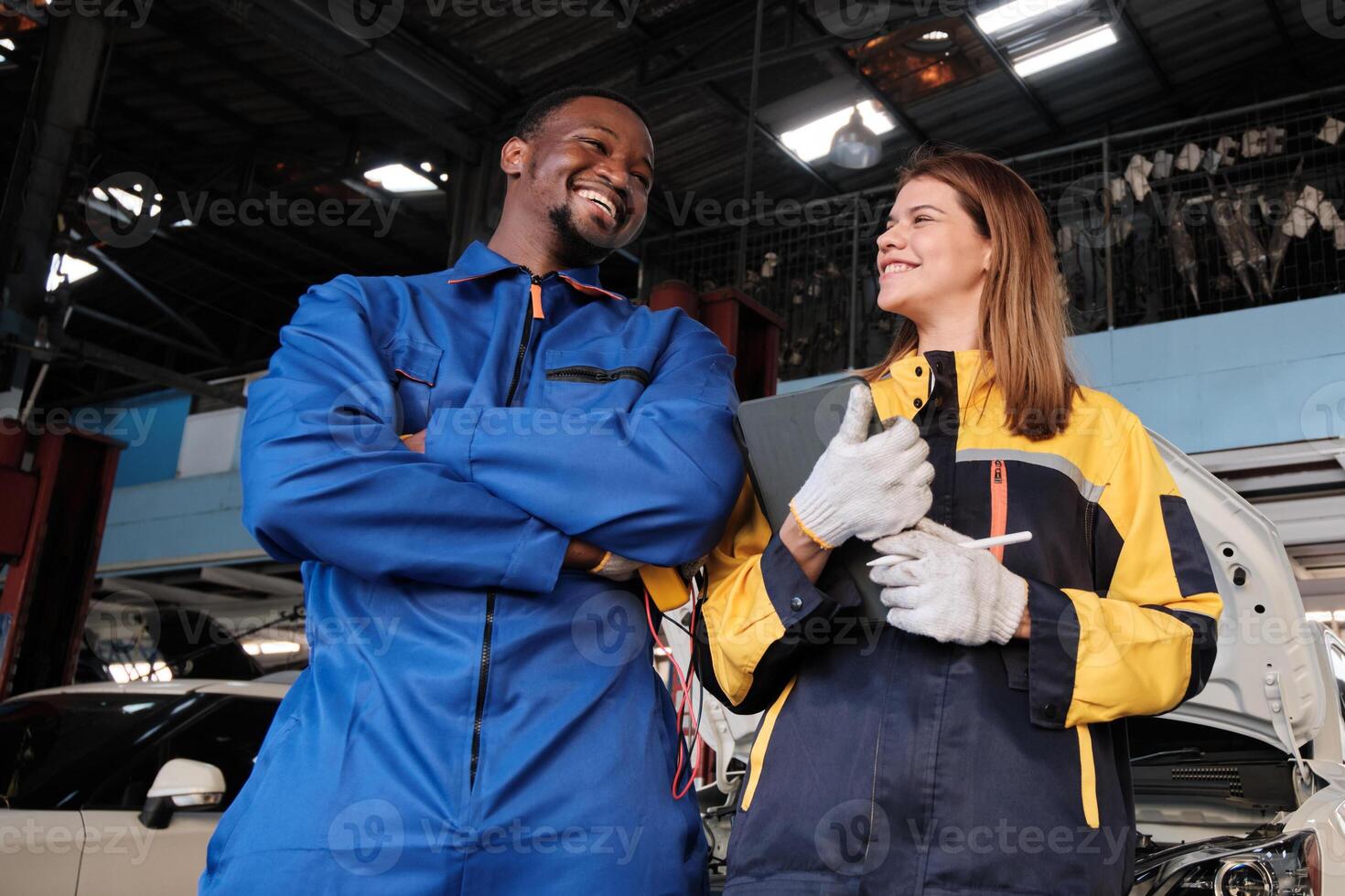 Two diverse mechanic coworkers, Black and White engineer partners, were cheerful and teasing, car check and maintenance service at a fixed auto garage, a professional transportation industry business. photo
