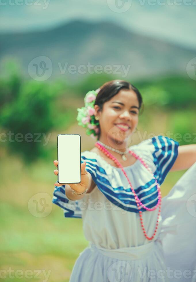 Portrait of Nicaraguan girl in traditional folk dress showing telephone screen. Young latin woman in traditional folk costume showing screen phone photo