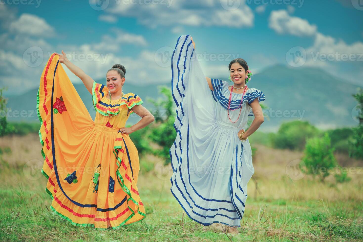 Portrait of two Hispanic girls wearing cultural folkloric costume in a field. Two happy Hispanic woman wearing cultural folkloric costumes outdoors photo