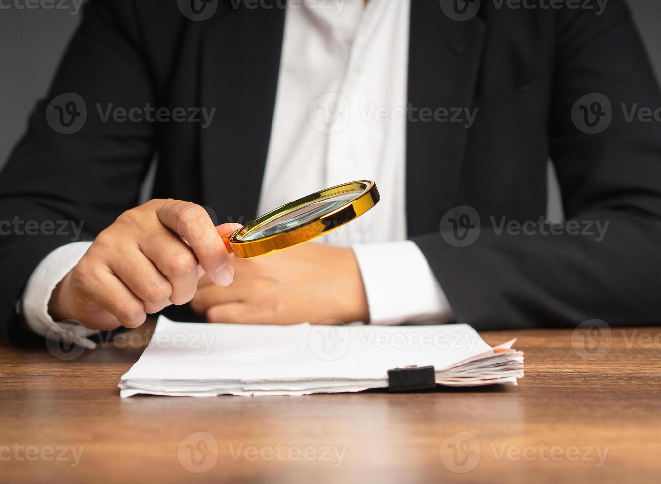 Businessman holding a magnifying glass and looking at reading documents while sitting in the office photo
