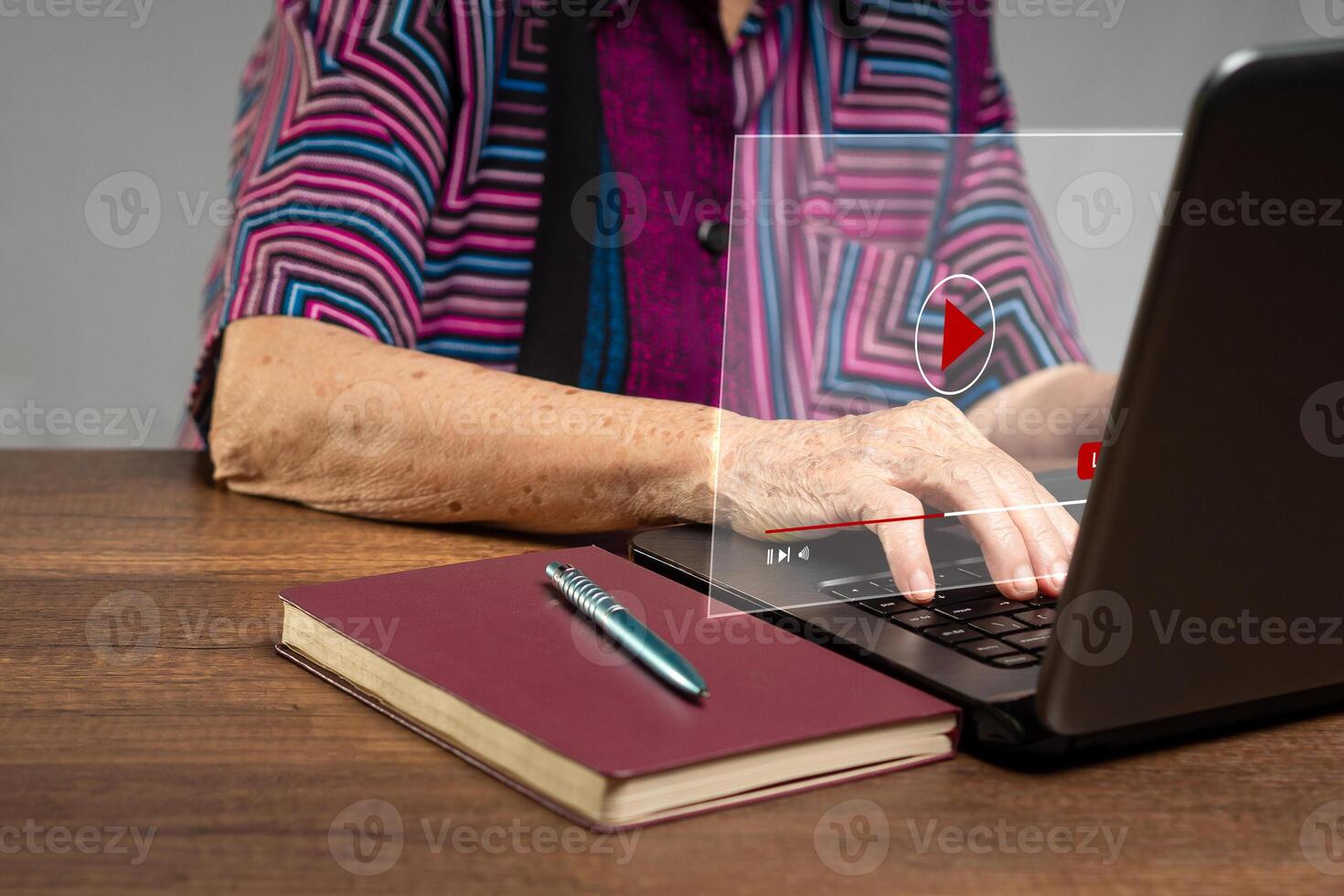Senior woman watches a live stream on a virtual screen with a laptop while sitting at the table photo