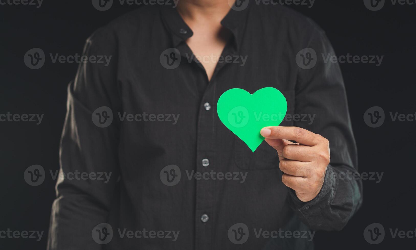 Hand holding a green heart shape symbol while standing against a black background. photo