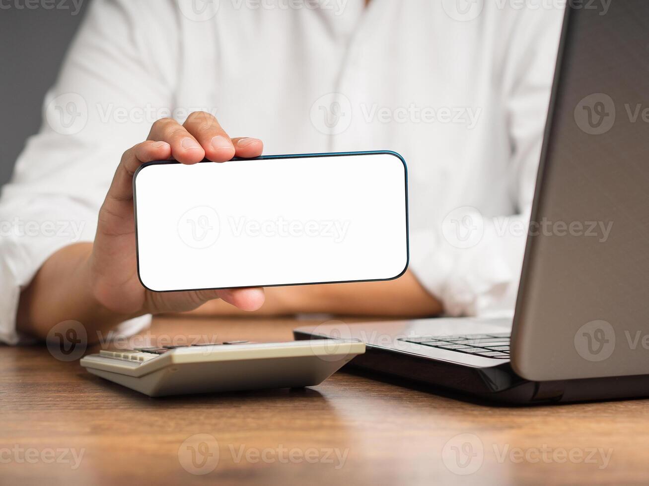 Businesswoman holding a white blank screen smartphone horizontally while sitting at the table photo