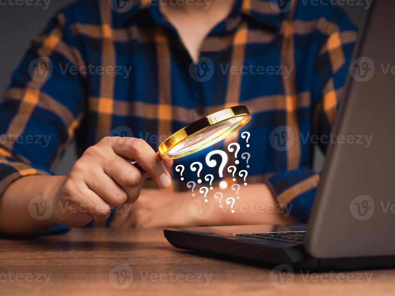 Close-up of a businessman is holding a magnifying glass and looking at a question mark symbol on a laptop while sitting in the office photo
