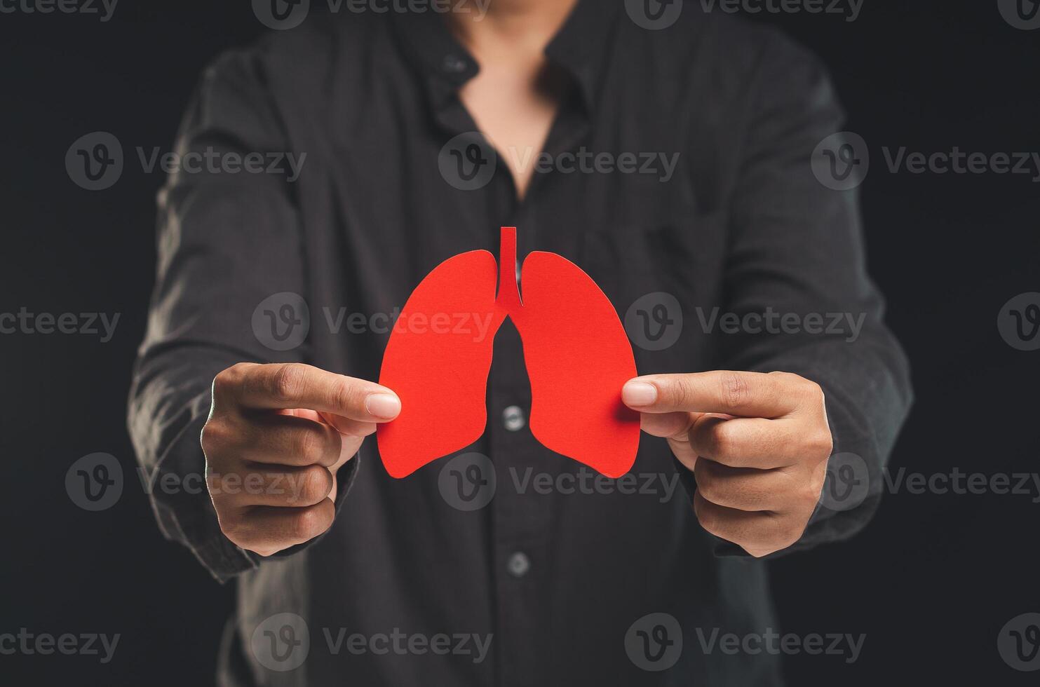 A man holding a lung shape symbol while standing on a black background. photo
