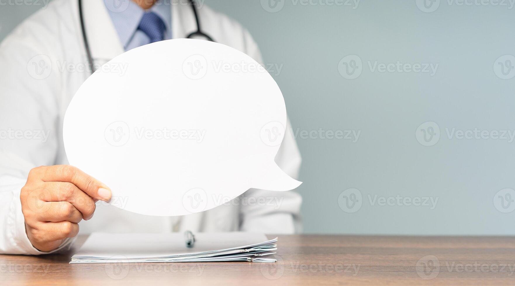 Close-up of a doctor holding a blank speech bubble while sitting at the table in the hospital. photo