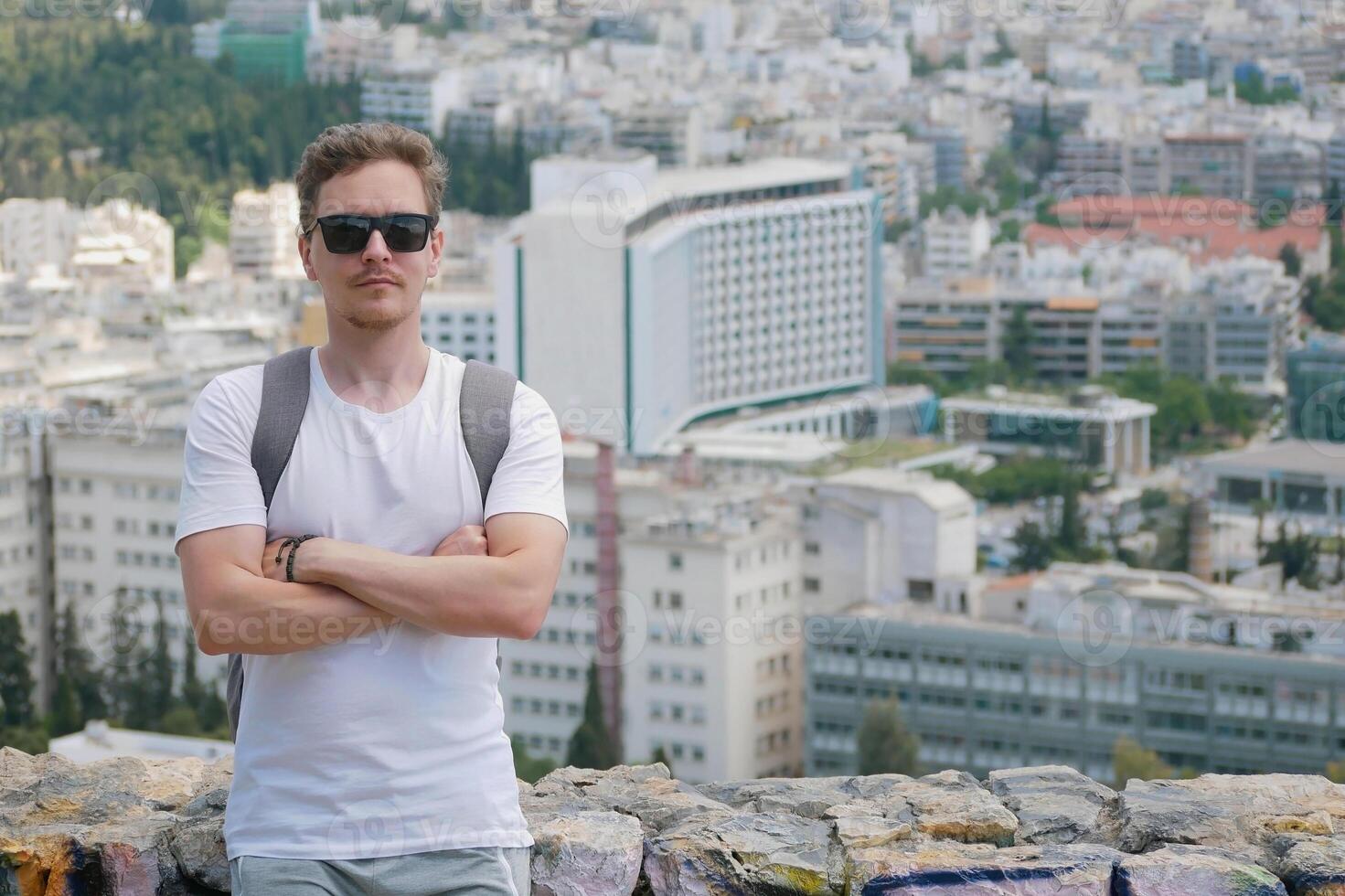 A man tourist with a backpack at the background of the panorama of the city of Athens at the observation deck. Front view. Travel touristic concept photo