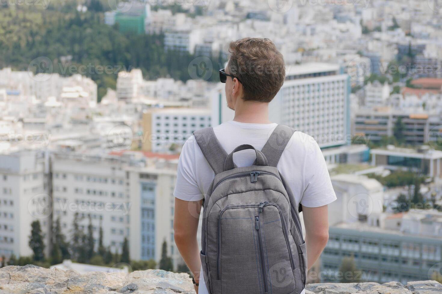 A man with a backpack looks at the panorama of the city of Athens from the observation deck. View from behind. Travel touristic concept photo