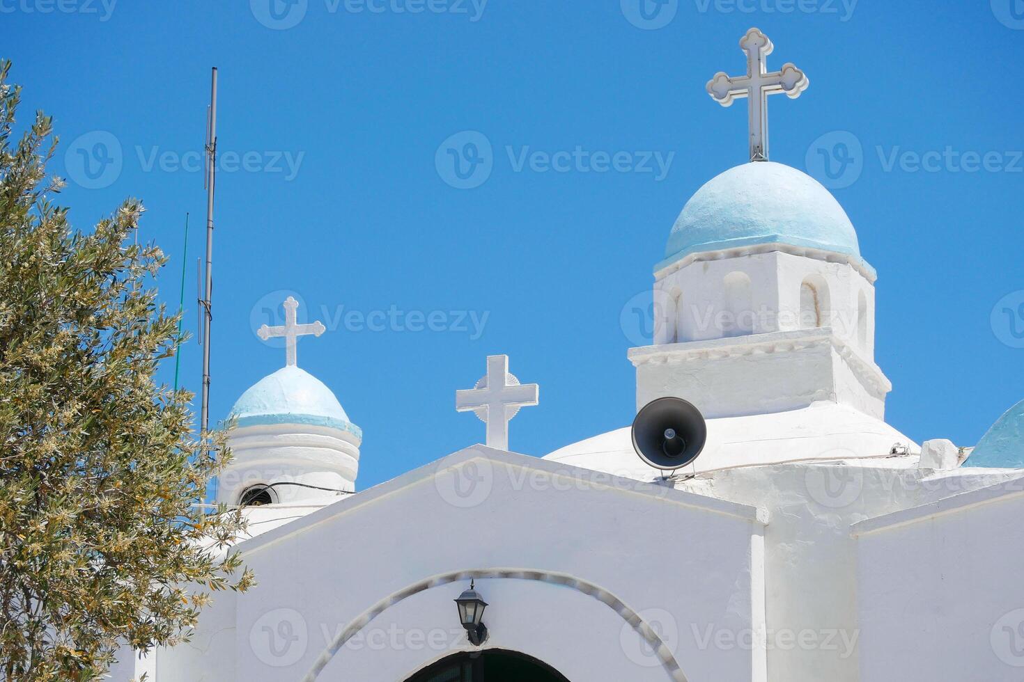 Traditional Greek Orthodox Church at the Lycabettus hill in Athens. Blue dome and white crosses close-up against sky with olive tree on the side photo