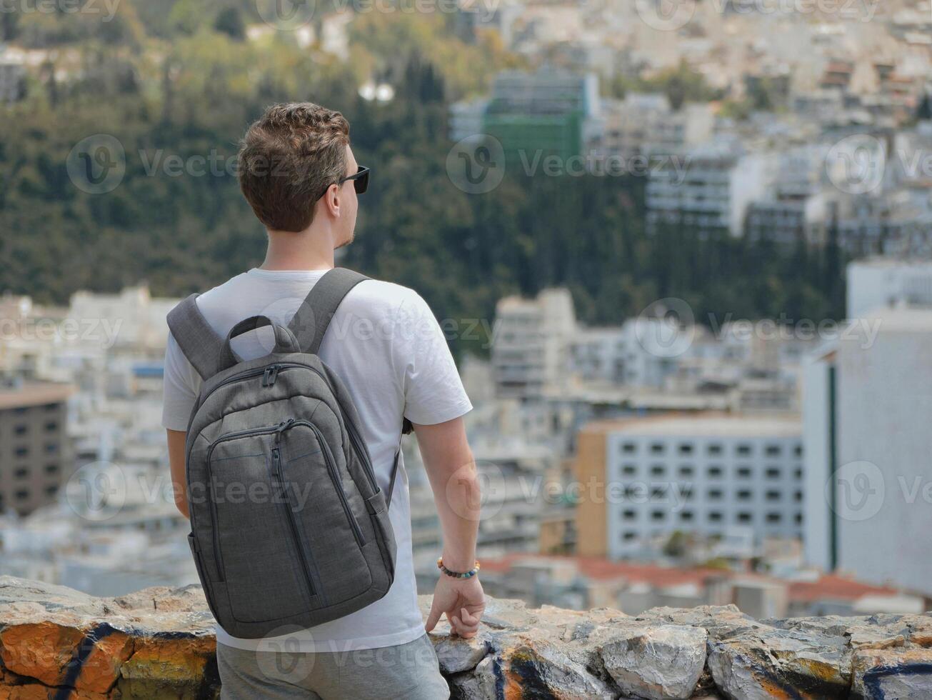 A man tourist with a backpack looks at the panorama of the city of Athens from the observation deck. View from behind. Travel touristic concept photo