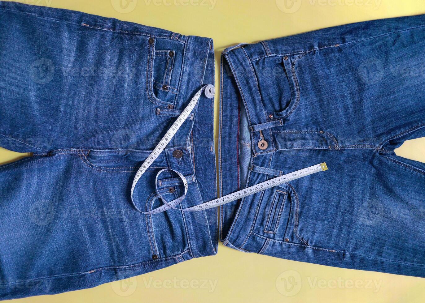 Two female blue jeans different size with measuring tape flat lay on a yellow background. Losing weight, overweight and healthy lifestyle concept photo