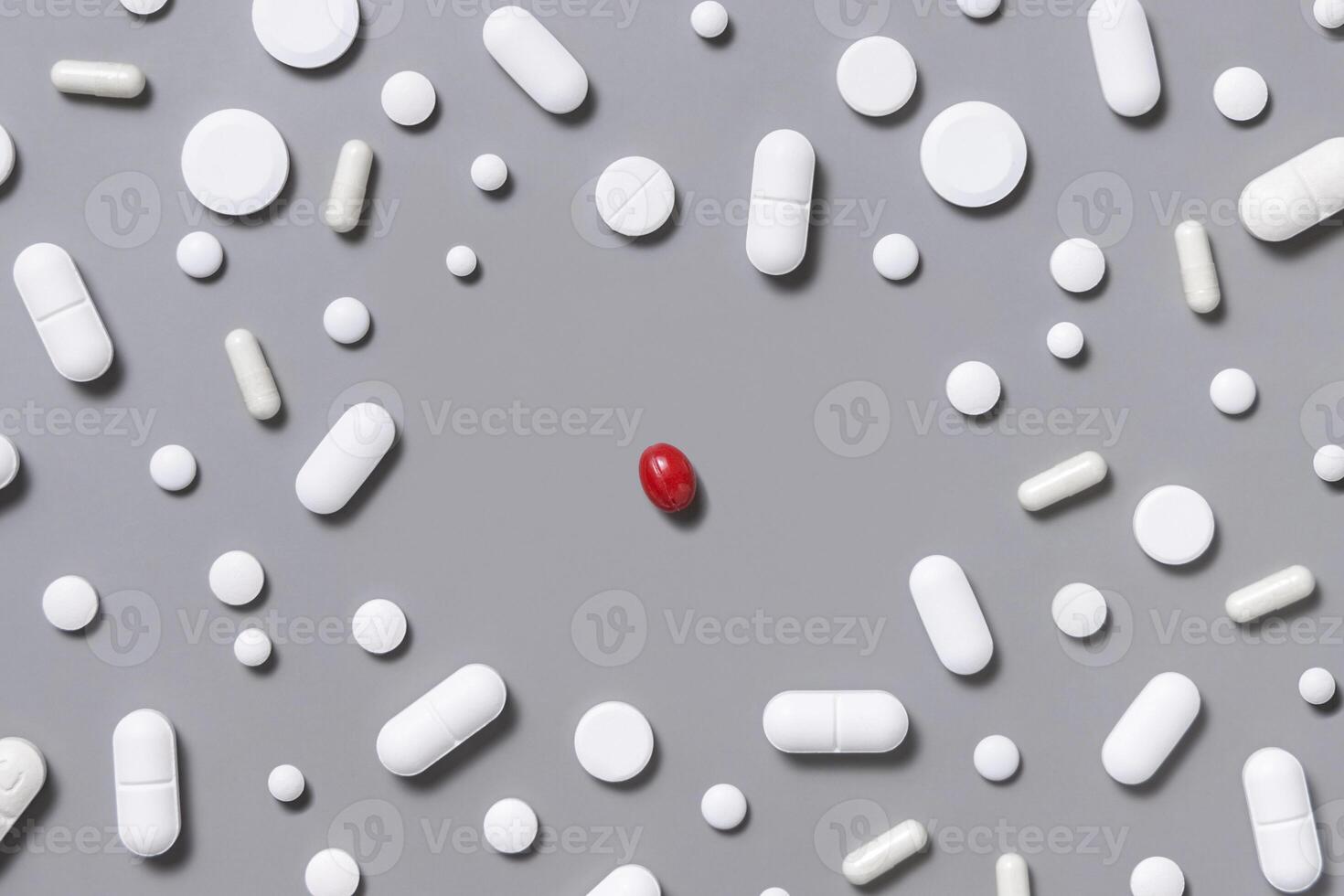 White medical capsules and pills with one red capsule in the middle on grey top view photo