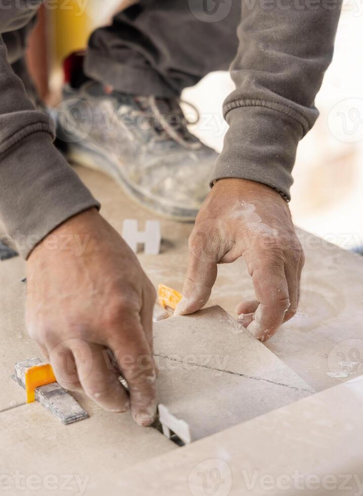 Tiler laying the ceramic tile on the floor with dusty hands. Home renovation or building a new house photo