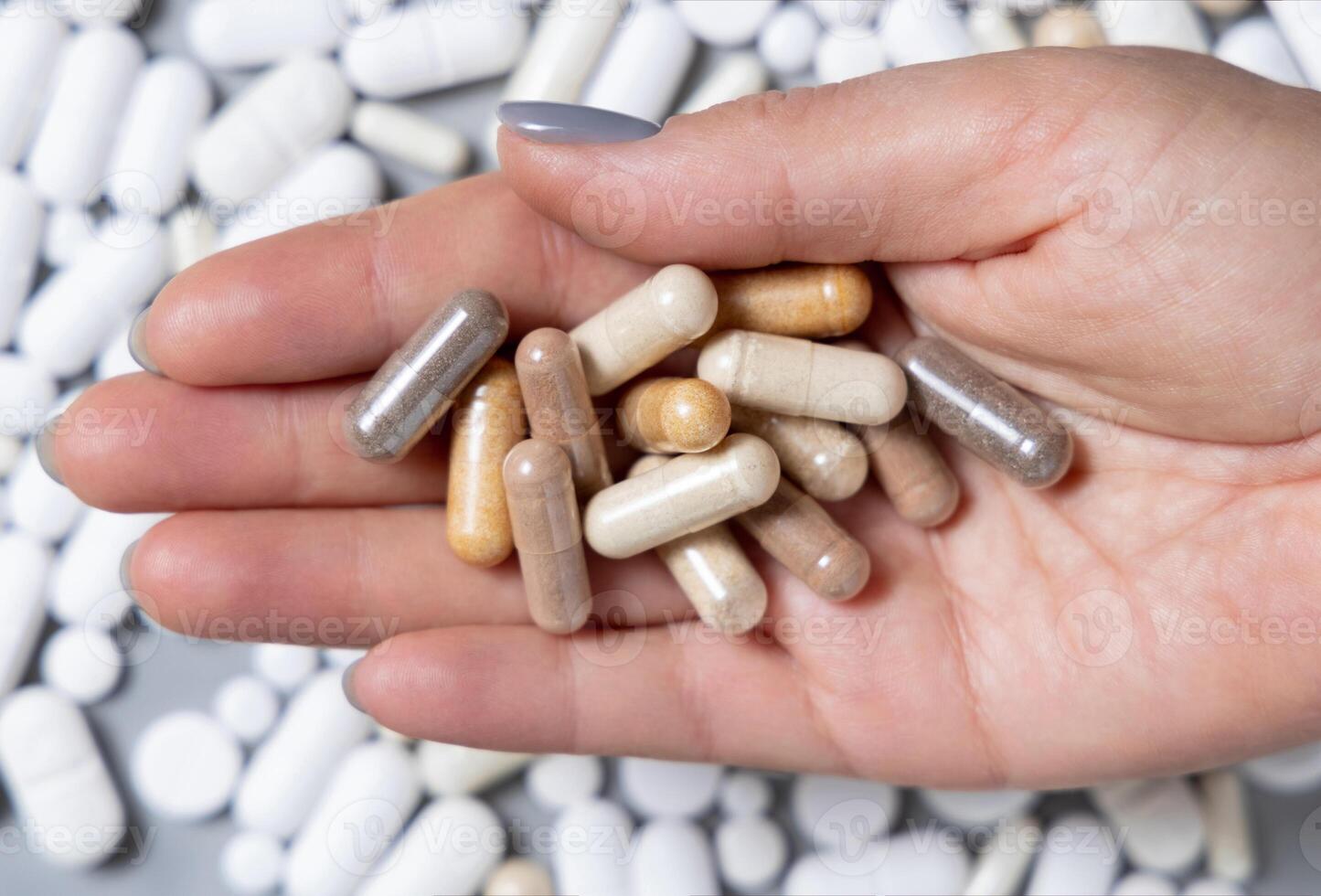Hand with mixed brown and beige medical capsules over mix of white pills, topview. Dietary supplements photo