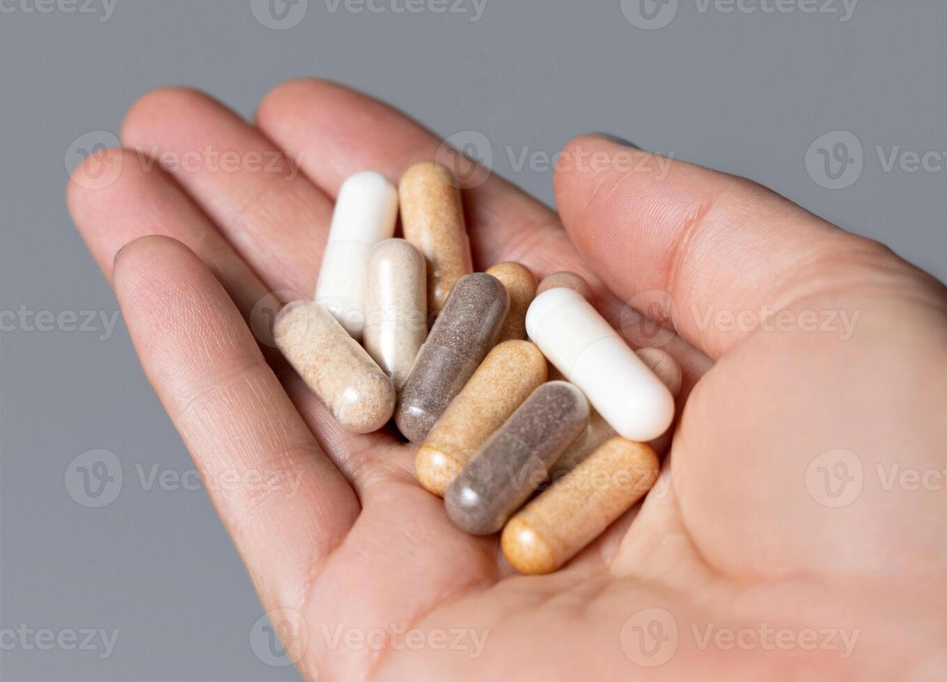 Cupped womans hand with a mix of beige and brown medical capsules closeup over grey photo