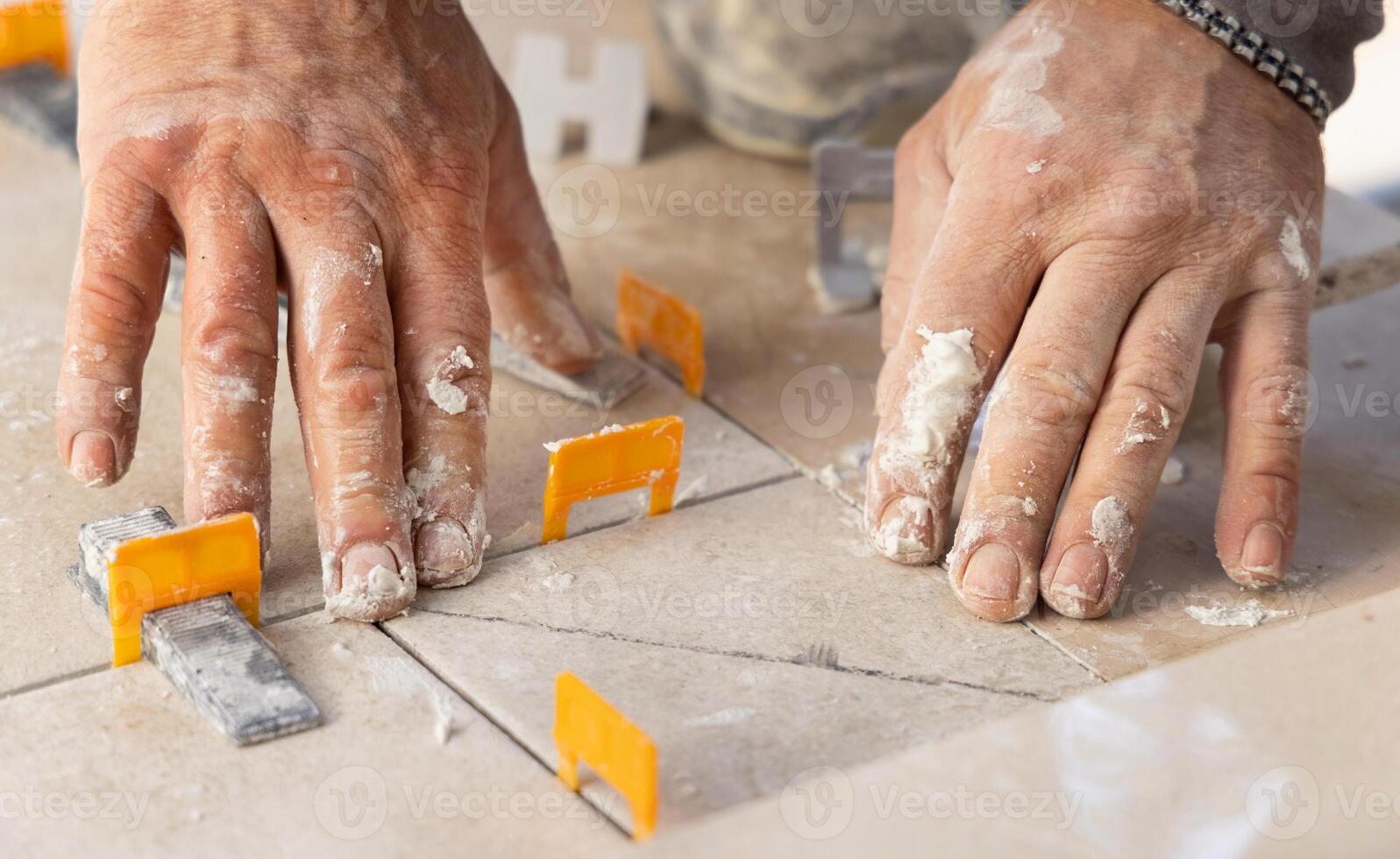 Tiler laying a ceramic tile on the floor with dusty hands. Home renovation or building new house photo