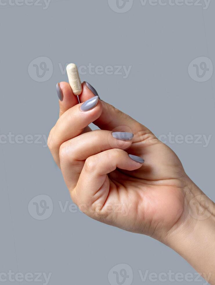 Female hand holding beige capsule with fingers closeup against grey, Healthcare concept photo
