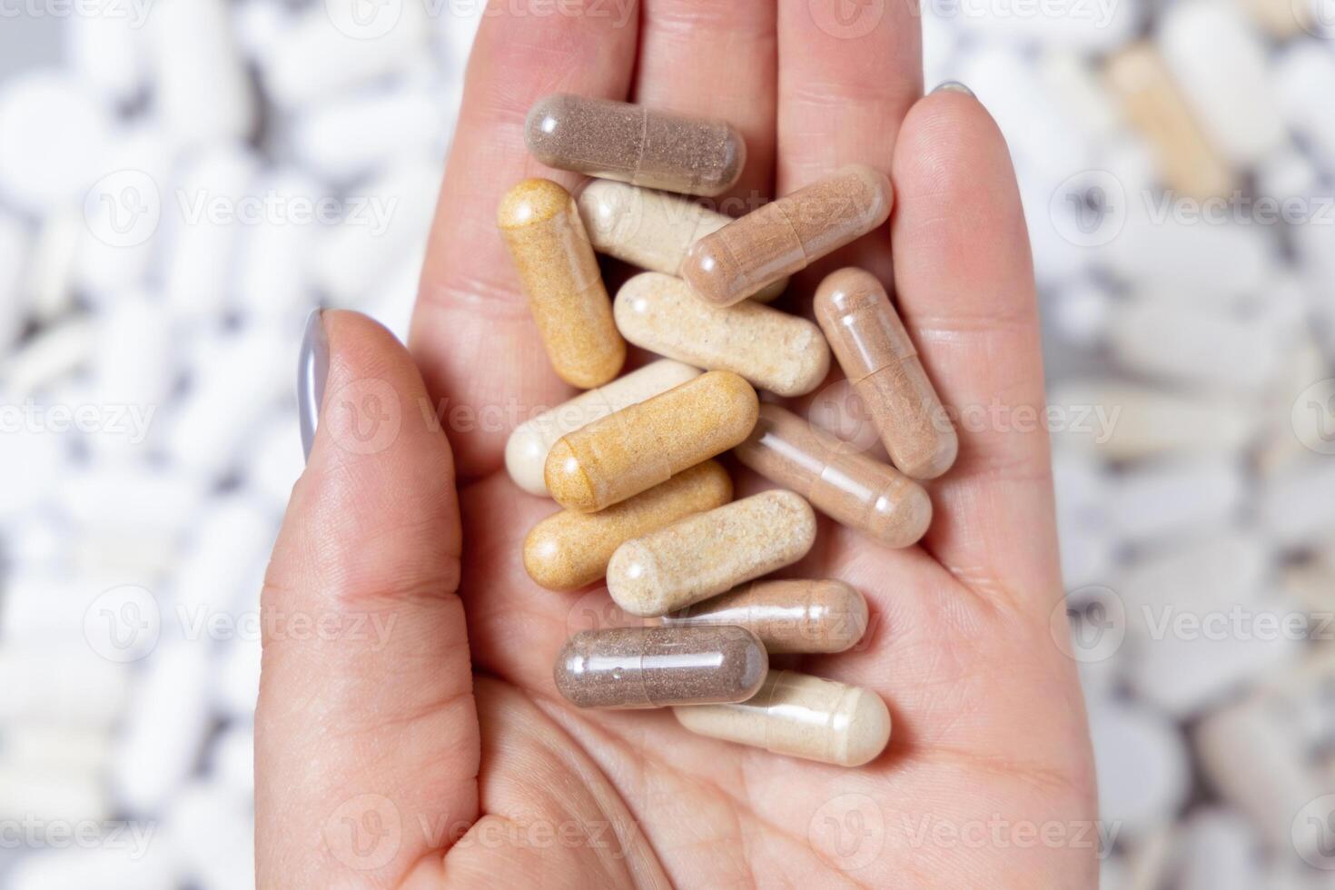 Hand with mixed brown and beige medical capsules over mix of pills top view. Dietary supplements photo