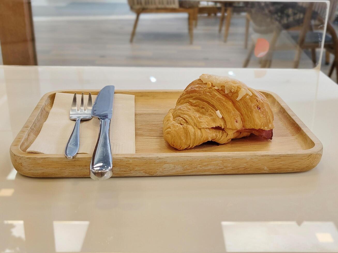 Ham cheese croissant with fork and knife on paper in rectangle wood plate on table. photo