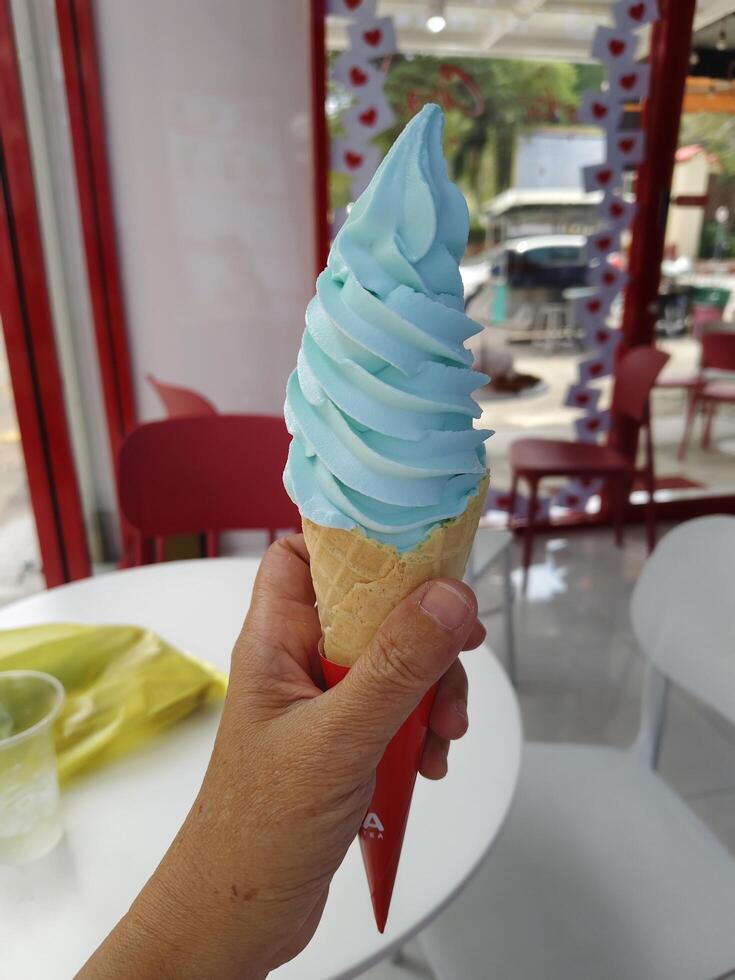 Left lady hand holding light blue salty ice cream cone in Thailand. photo