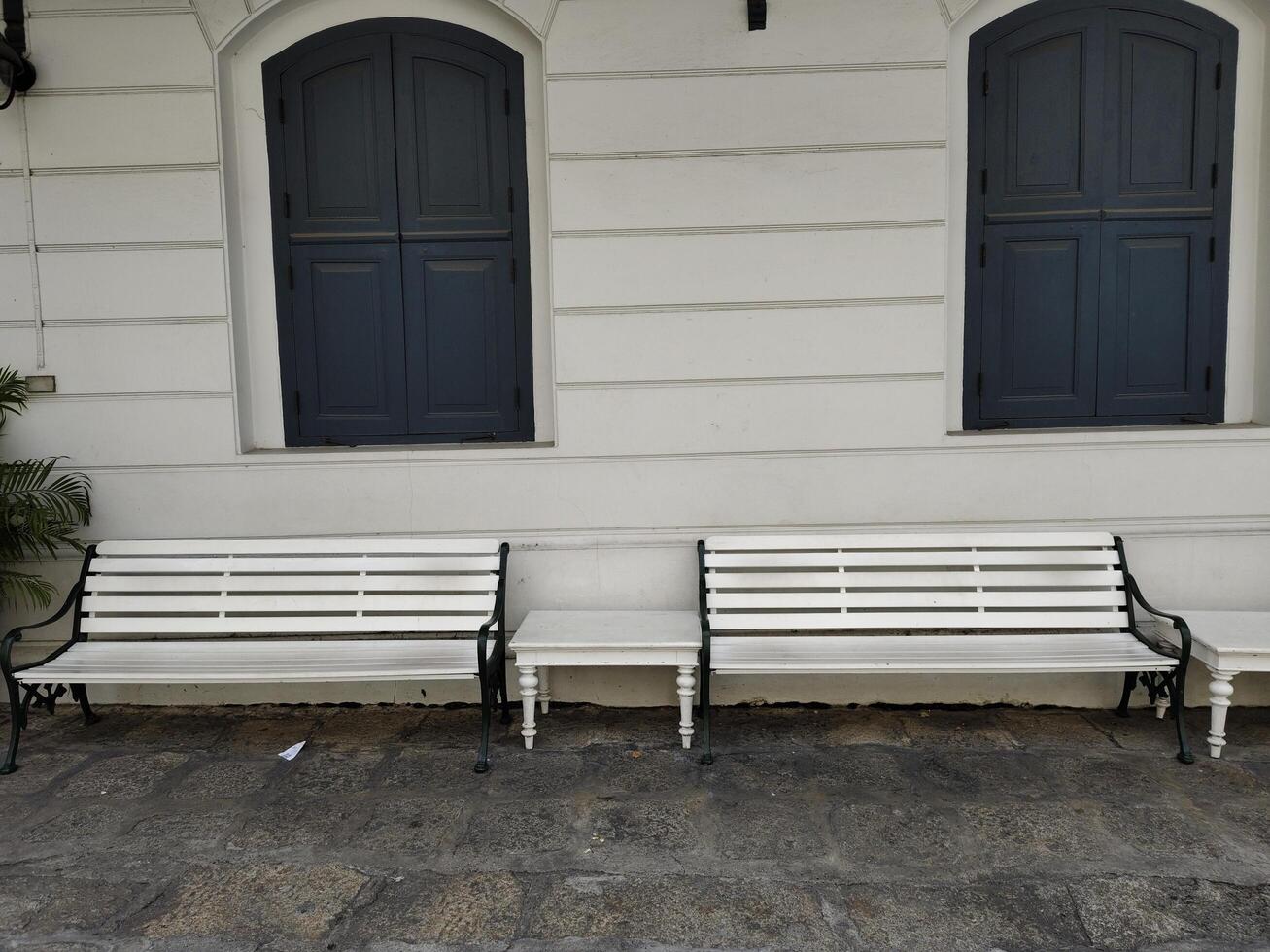 White benchs on concrete floor and white wall with closed windows of building in retro style in Thailand. photo