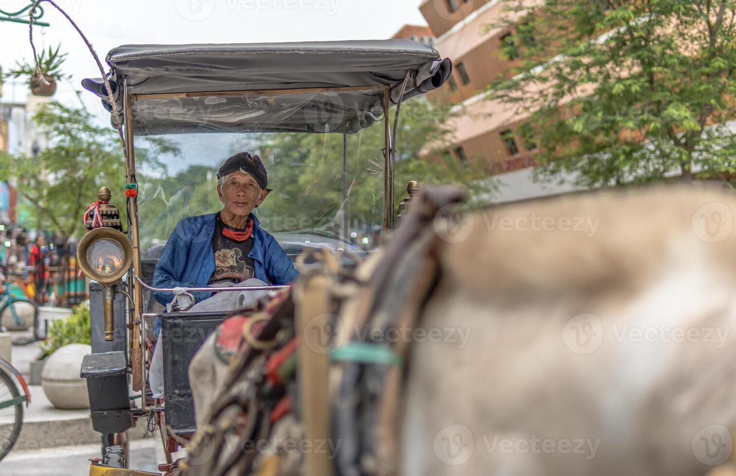 An elderly man in traditional attire driving a horse-drawn carriage in Yogyakarta photo