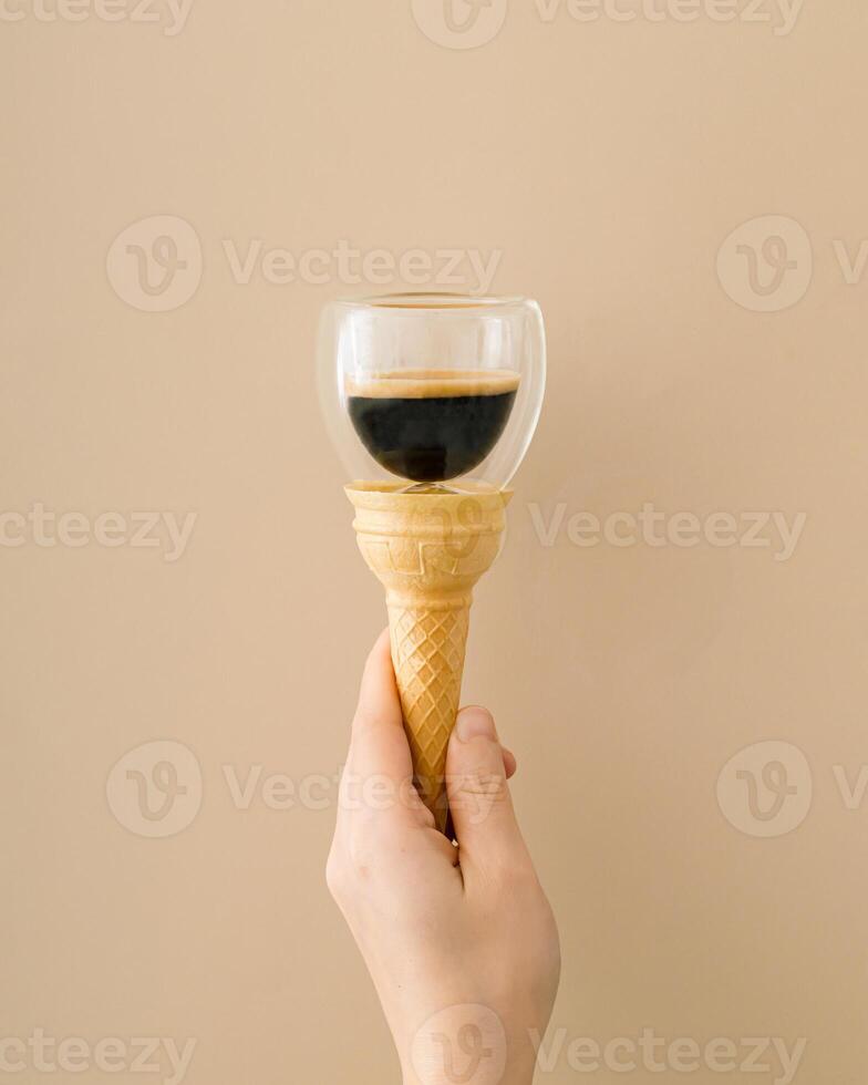 A unique conceptual photo of female hand holding an ice cream cone with cup of coffee on beige background. Minimal surreal food and drink concept. Trendy ice cream idea. Coffee aesthetic.
