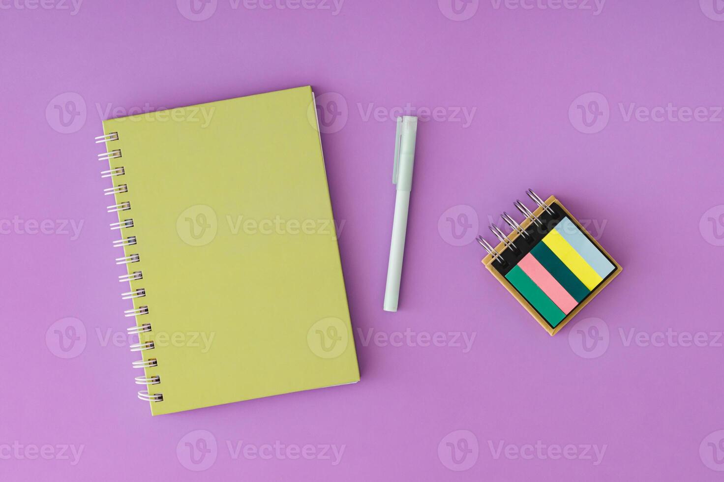 Green spiral notebook and pen on a vibrant purple background. Trendy composition ideal for creative workspaces, office themes or back to school concepts. Minimalistic colorful office desk flat lay. photo