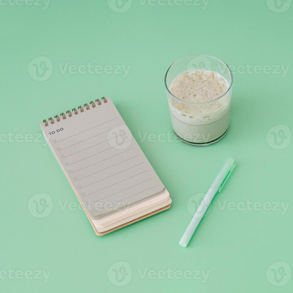 To do list in spiral notepad with iced matcha latte. Trendy pastel green background. photo