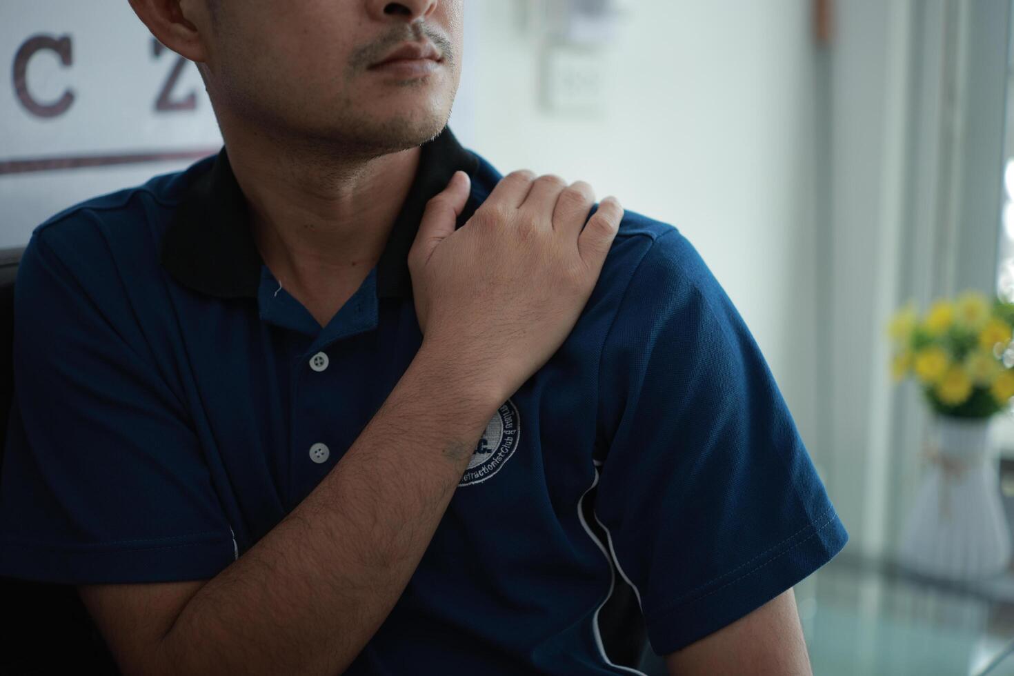 a man in a blue shirt holding his shoulder photo