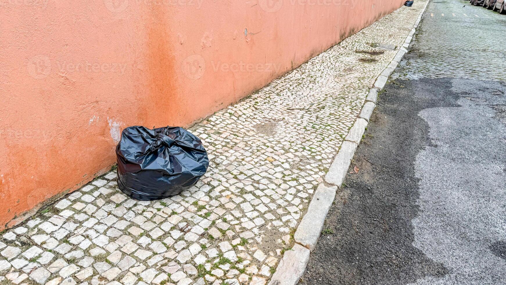 Black garbage bag on cobblestone street whispers tales of urban solitude, embracing Unplugging Day, hidden narratives of routine neglect photo