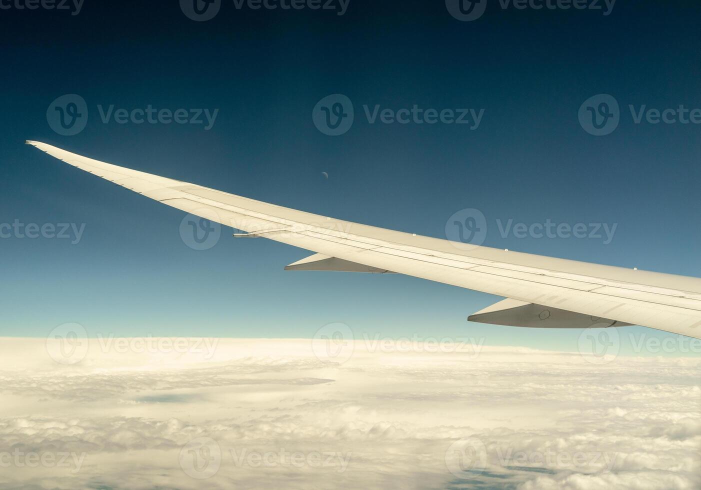 Airplane wing view above the clouds with distant moon photo