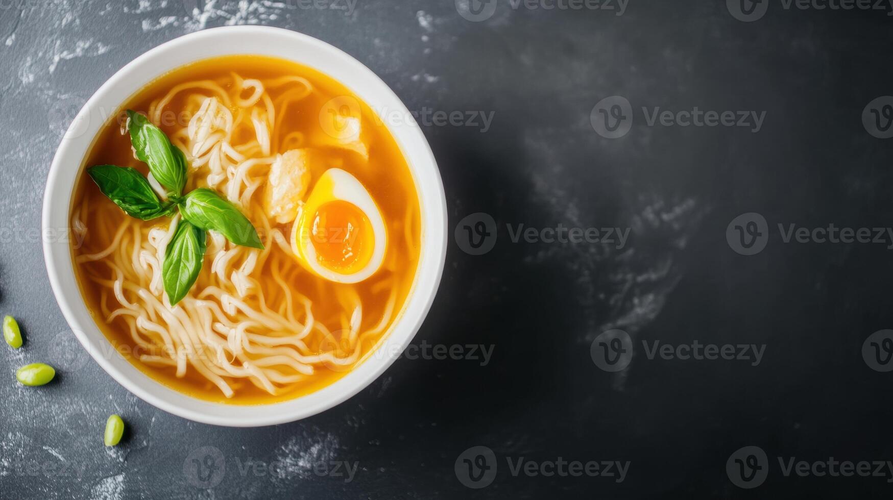 Bowl of steaming chicken noodle soup with soft boiled egg and fresh basil leaves on dark textured background, comforting hot meal in a white ceramic bowl photo